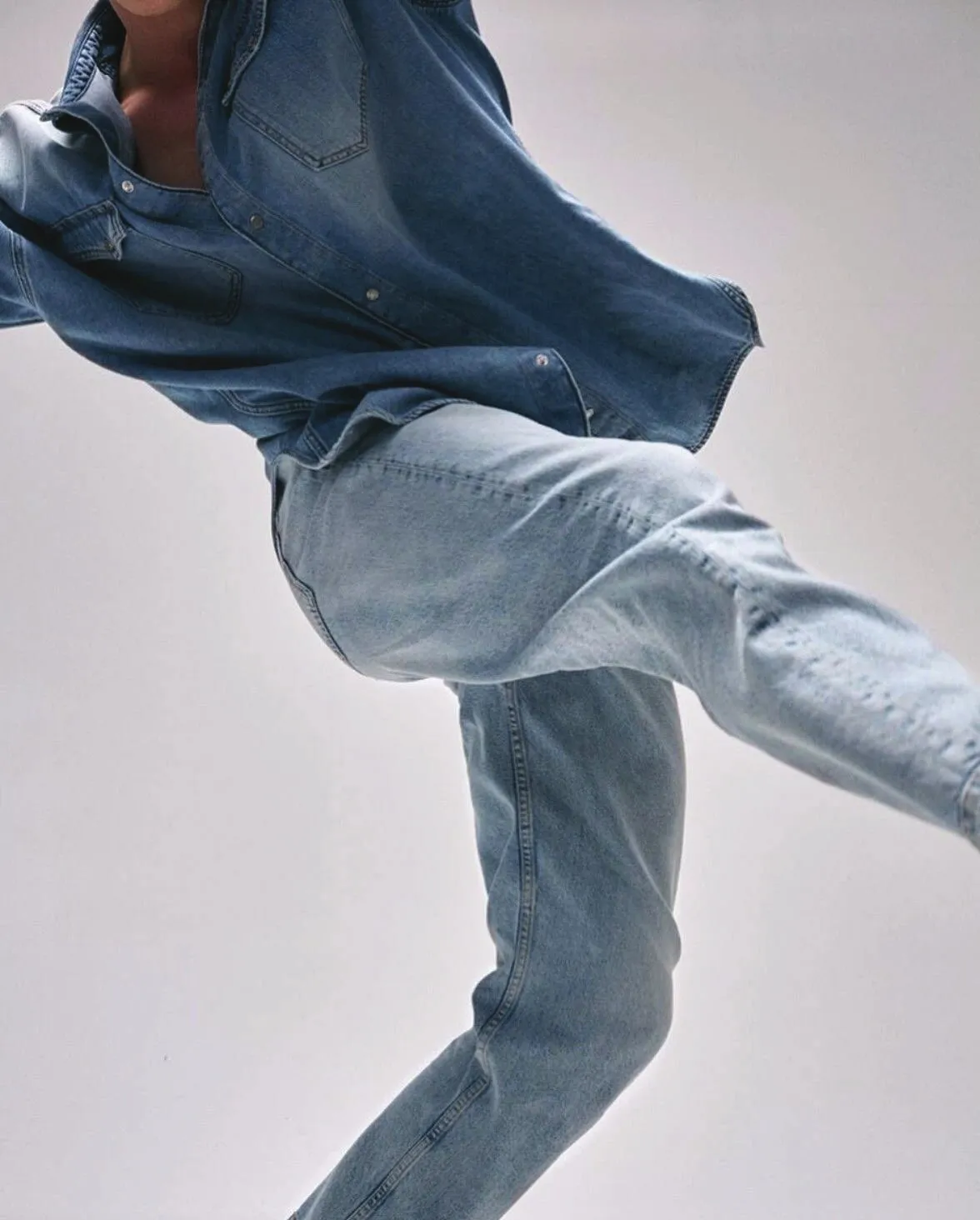 Model mid-stride in light-wash jeans and an oversized denim shirt