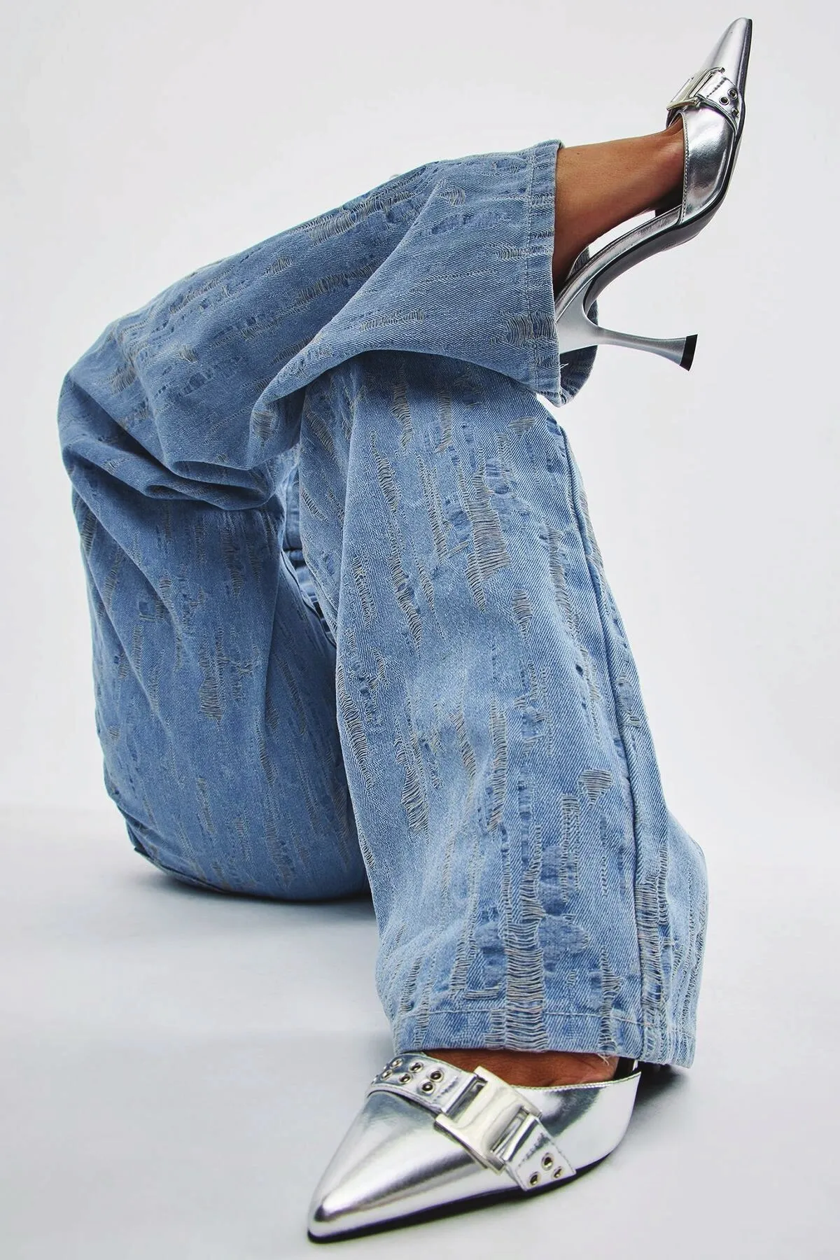 Close-up of mid-wash flare jeans over silver heels