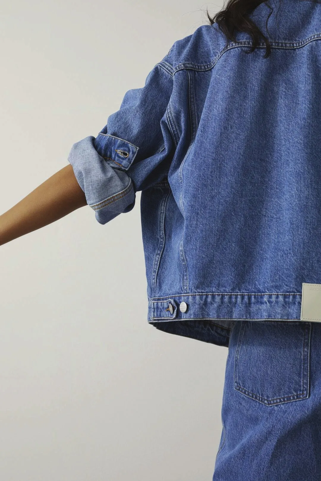 Model in a mid-wash denim jacket with rolled sleeves, arm outstretched